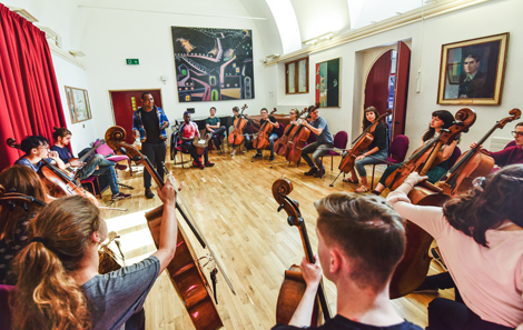In the Weston Gallery with colourful artwork on the walls, student cellists line the walls as the Manchester Collective's Abel Selaocoe  inspires them 