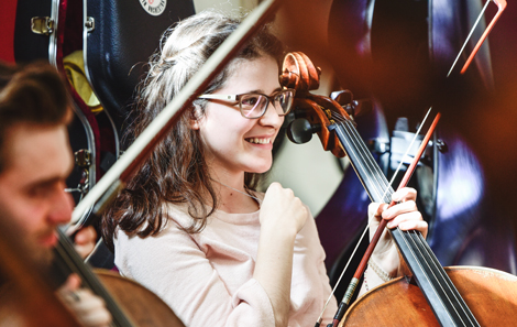 surrounded by cellos, a femal student looks delighted to be in the workshop 