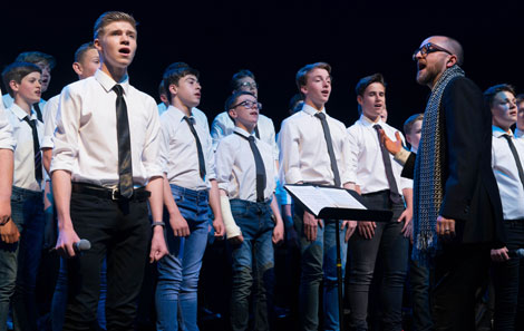 Tim stands in front of a choir of Only Boys Aloud conducting and singing along