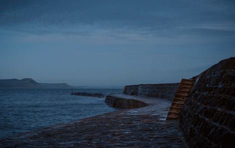 The Cobb at Lyme Regis, stone steps lead up to a sea wall on the one side. The other looks out on desolate sea 