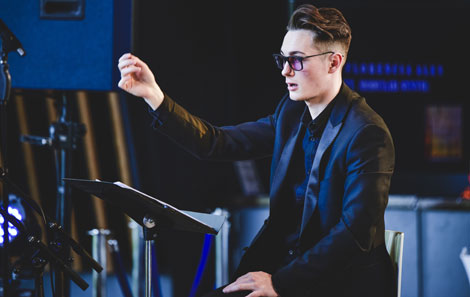 Jasper seated in front of a music stand with his one hand up, conducting the contemporary opera Spinning Jenny at the College's Atmospheres new music festival last year.