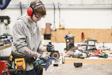 young man with ear protectors and goggles cutting through metal with a machine 