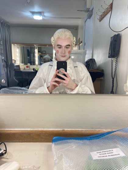 George, in character costuem with regency white wig and silk shirt, takes a selfie in front of the mirror in his dressing room 