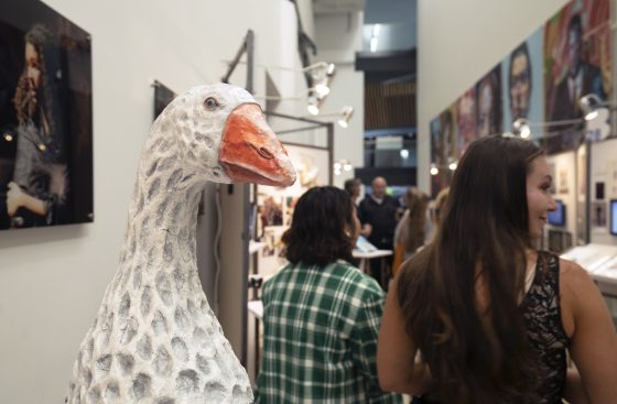 The corridor of the Balance exhibition. A huge goose with an orange beak is in the foreground, with members of the public walking by to look at the photos and pictures either side of it