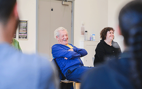 Ian McKellen leans back in his chair laughing at something the students in the room have said. Next to him, smiling is Alice White, head of voice. 